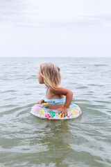 Child girl in a swimsuit with a circle bathes in the sea.
