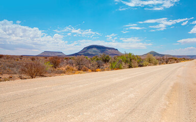 Beautiful empty gravel dirt road in desert plain with mountains in background - Namibia, Africa