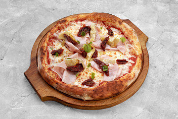 pizza with veal, ham, cheese and sun-dried tomatoes on a gray table