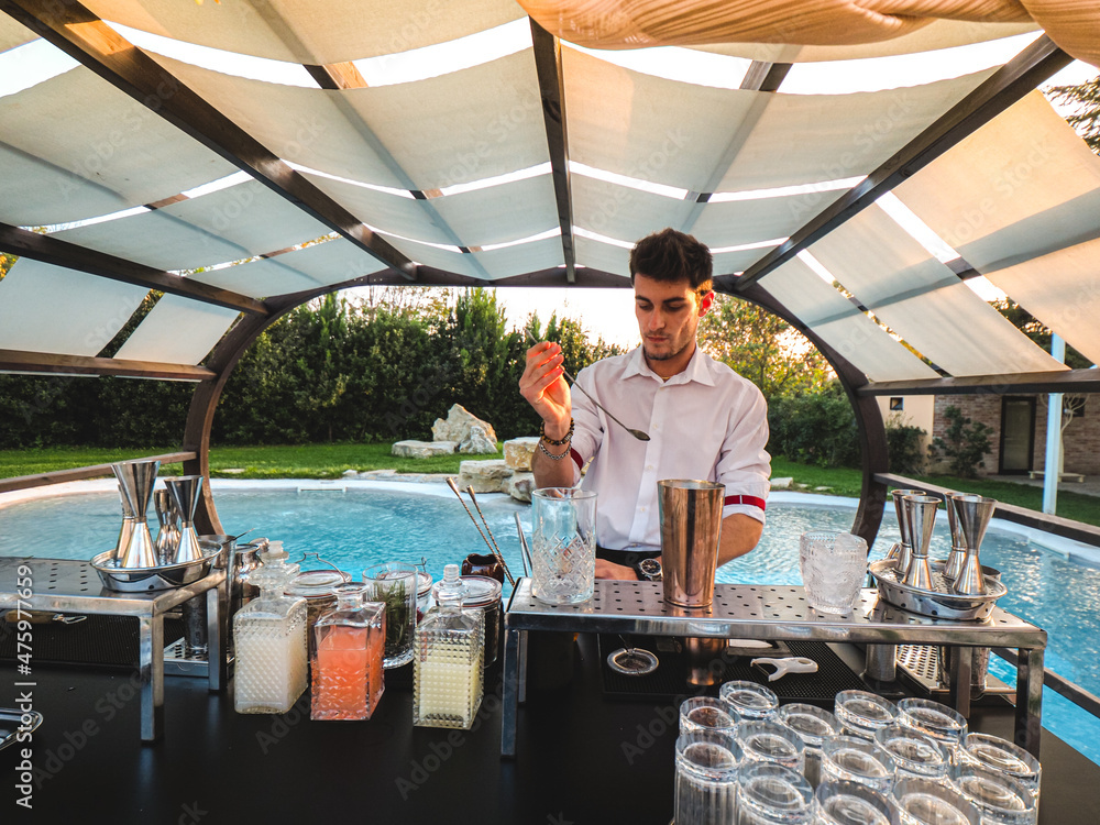 Poster young caucasian barman making a refreshing cocktail outdoors by the pool at an event