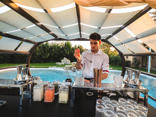 Young Caucasian barman making a refreshing cocktail outdoors by the pool at an event - Powered by Adobe