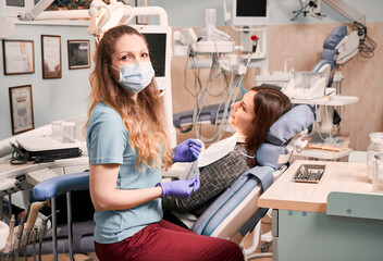 Female dentist holding explorer and mirror while woman lying in dental chair. Stomatologist looking...