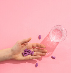 handful of tablets in the palm of your hand next to a glass of water