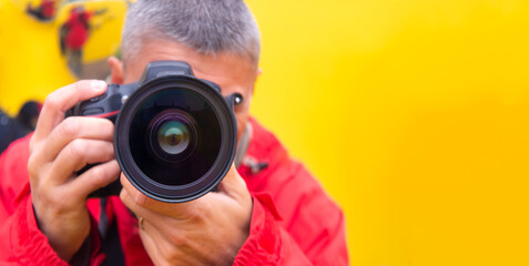 Front view of photographer hands on camera. A man wearing red jacket on a yellow background.