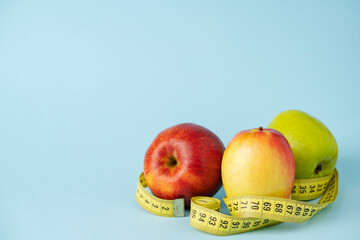 Green and red apple wrapped with tape measure, on blue background.