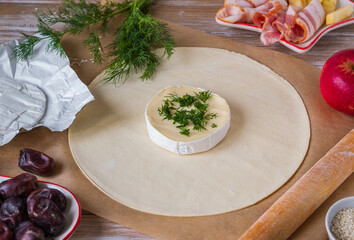 Step by step cooking of baked camembert in puff pastry with bacon, date and apple on a wooden...
