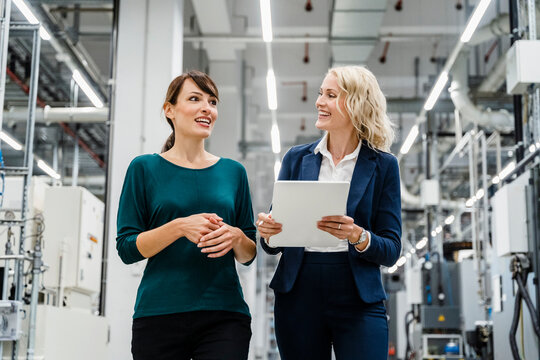 Smiling businesswomen discussing at modern factory - Powered by Adobe