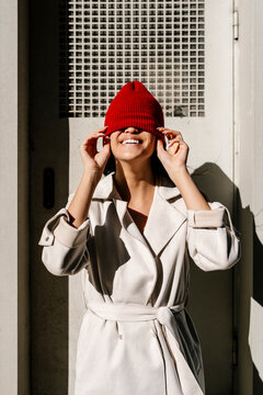 Playful woman covering face with knit hat on sunny day