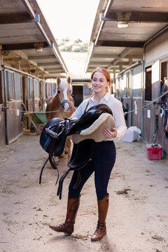 Thoughtful woman with saddle standing in stable