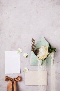 Studio shot of envelope, invitation card, tied bow and flowers flat laid against light pink background