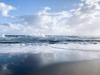 Seascape, white clouds on the blue sky reflection, sea surface, sand beach