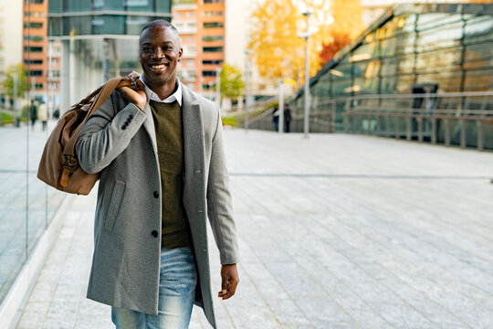 Smiling businessman with duffel bag walking on footpath
