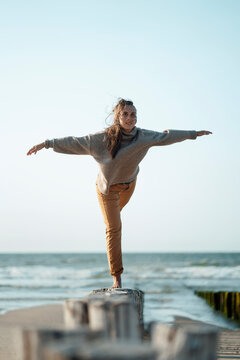 Woman with arms outstretched balancing on wooden post at beach