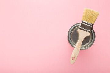 New brush and metal can of paint on light pink table background. Pastel color. Closeup. Preparation for repair work of home. Empty place for text. Top down view.