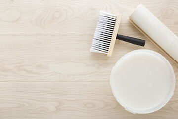 Roll of wallpaper, brush, bucket with glue on light wooden table background. Closeup. Preparation...