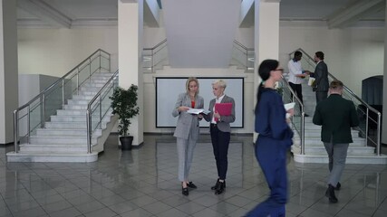 Wide shot portrait busy professional women discussing business project with colleagues passing greeting around in office lobby. Concentrated coworkers planning project indoors. Lifestyle and success