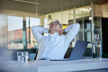 Smiling businessman relaxing while sitting on chair at workplace