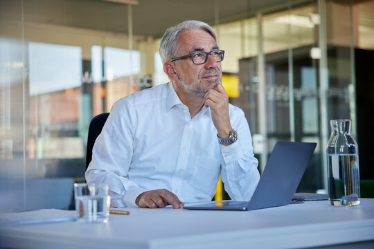 Mature businessman with laptop contemplating at workplace