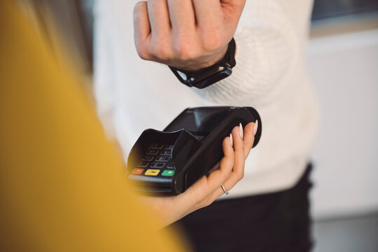 Man paying through smart watch to waitress holding credit card reader in cafe