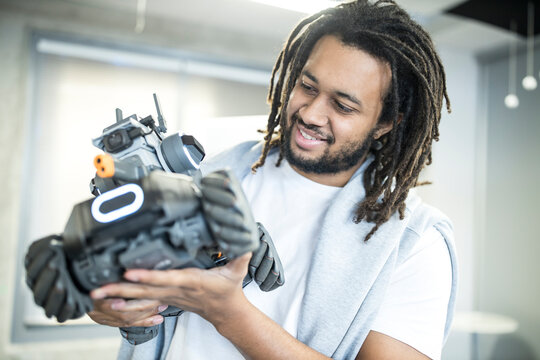 Smiling technician looking at robotic combat tank model in workshop