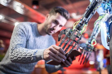 Technician with tablet PC holding robotic arm at workshop
