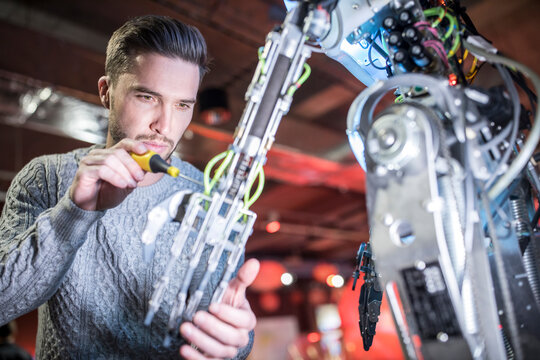 Concentrated engineer fixing robotic arm with screwdriver at workshop