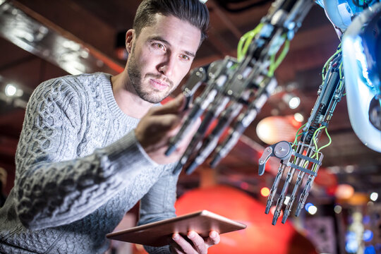 Engineer examining robotic arm holding tablet PC at workshop