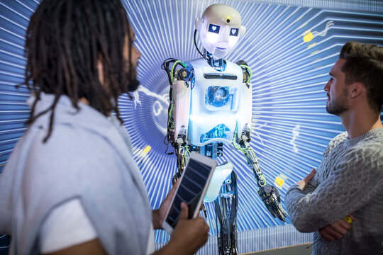 Technician with colleague holding tablet PC looking at human robot in workshop