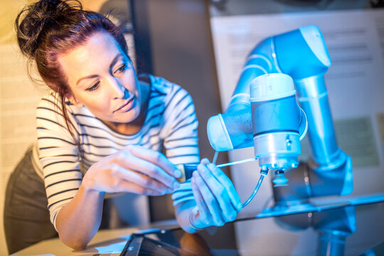 Technician repairing robotic arm with screwdriver leaning on table at workshop