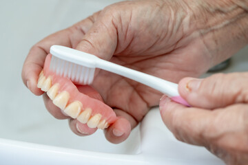Asian senior or elderly old woman patient use toothbrush to clean partial denture of replacement...