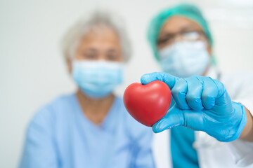 Doctor wearing ppe with mask hold red heart for protect coronavirus with Asian senior or elderly old woman patient