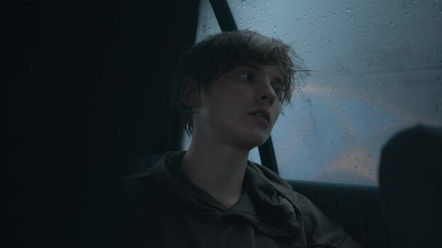 Hipster-looking young man sits in a car in the rain and gives an interview into the lavalier microphone attached to clothes