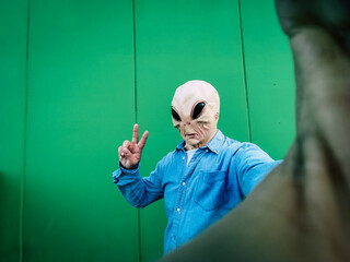 Standing alien mask face taking selfie picture against green background wall. Copy space for comic...