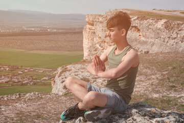 Sports man practices yoga on the top of the mountain. Meditation and exercise in nature.