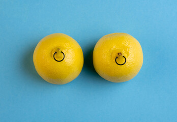 Lemons in shape of woman breast with nipple piercing on blue background.