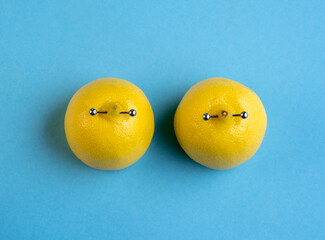 Lemons in shape of woman breast with nipple piercing on blue background.