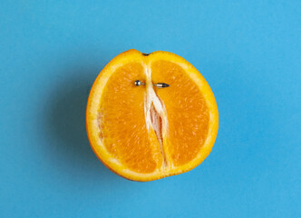 Half an orange with  vertical barbell piercing on a blue background. - obrazy, fototapety, plakaty