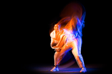 Sportive young girl in white costume dancing hip-hop dance isolated on dark background at dance...