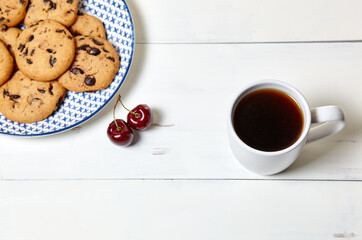 White cup with coffee, traditional cookies and sweet cherries on a white wooden background, closeup. Tasty breakfast, morning routine concept