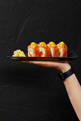 Female hand holding plate with sushi rolls with seared salmon, cream cheese, red tobiko and mango