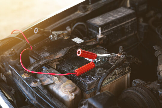 Charging old car battery by using electricity trough red and black jumper cables. Car maintenance concept.