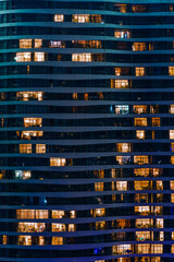 Glass facade of modern city high rise, buildings show lighting using by human activity, energy usage at night time. Glowing windows of skyscrapers at night.