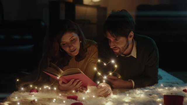 Ragazzo e ragazza su tappeto bianco per San Valentino con cuore in filo di luci led legge libro