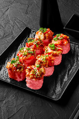 Sushi rolls in mamenori with fried shrimp, bell pepper, scallions with soy sauce on black plate