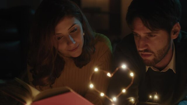 Ragazzo e ragazza su tappeto bianco per San Valentino con cuore in filo di luci led legge libro
