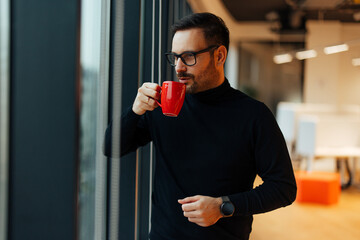 Calm caucasian man, taking a sip of his coffee, during a work break.