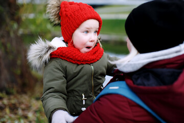 Young mother holding her funny surprised daughter on hands, walking outdoors