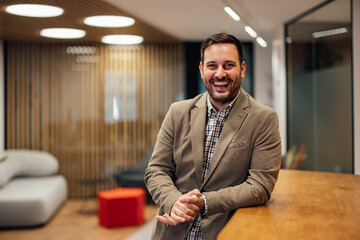 Portrait of smiling adult man, leaning onto the reception desk in the company lobby.