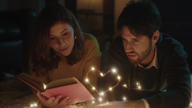 Ragazzo e ragazza su tappeto bianco per San Valentino con cuore in filo di luci led legge libro