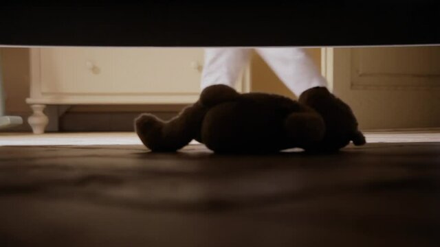 Slow motion closeup shot: a little girl finding her beloved teddy bear under the bed.
